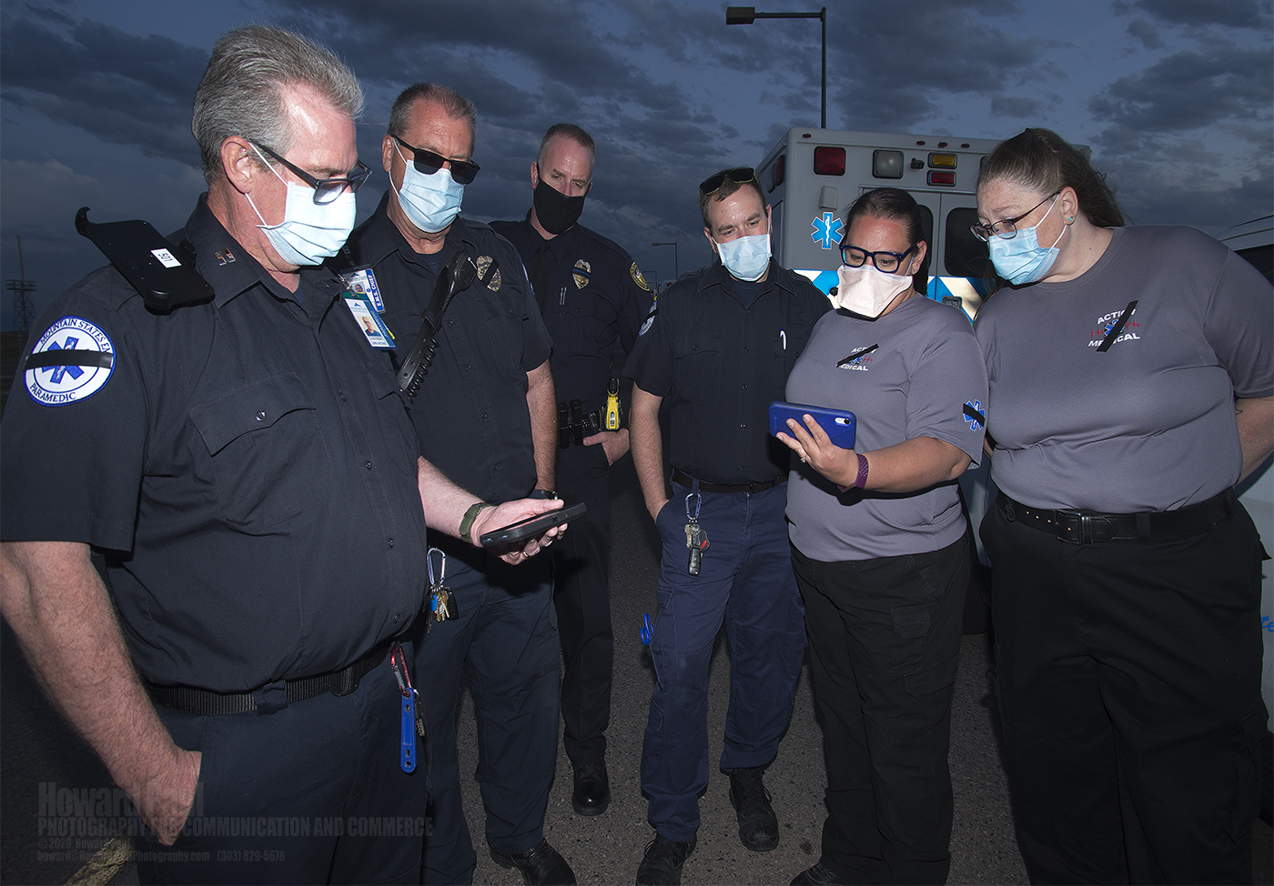 (L-R) Paramedic David Fending, Mountain States EMS, University of Colorado Police Department officers and Action Medical employees watch the 9News live aerial coverage of the coffin being removed from the United Airlines jet that transported Paul Cary’s remains.