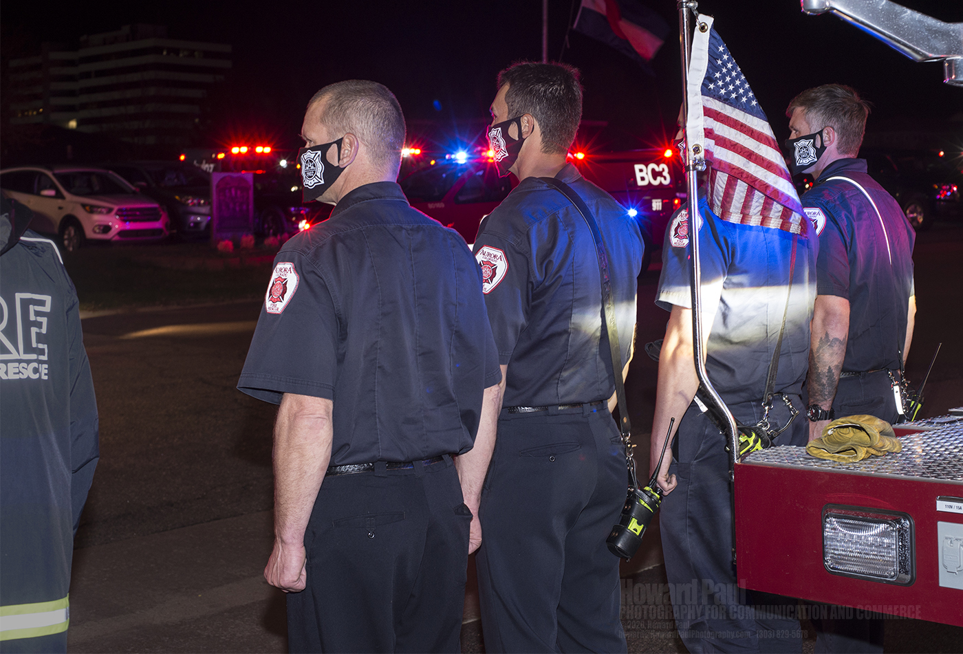 An Aurora Fire Department truck company at the entrance to the cemetery. AFD and Denver Fire Department aerial ladders flanked the entrance, with a large American flag suspended between them.